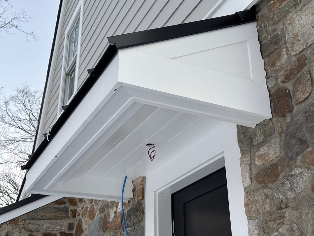 Custom entry portico Berwyn PA with white beadboard soffit, V-groove fascia panels, decorative bracket, and black metal drip edge on a stone home by D&E Mako Renovation