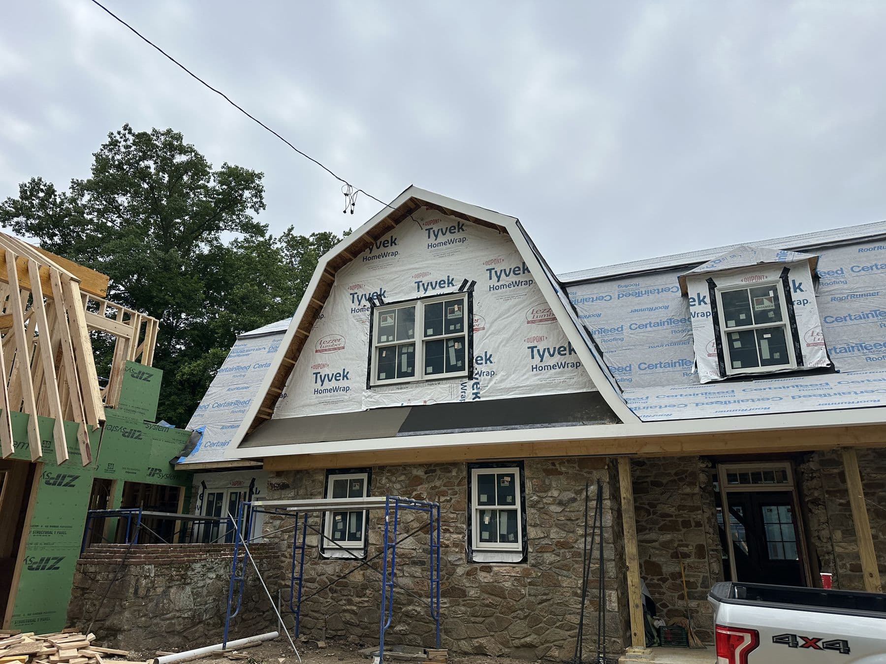 Stone gambrel house with the upper roof opened up and wrapped in housewrap before new dormers go in