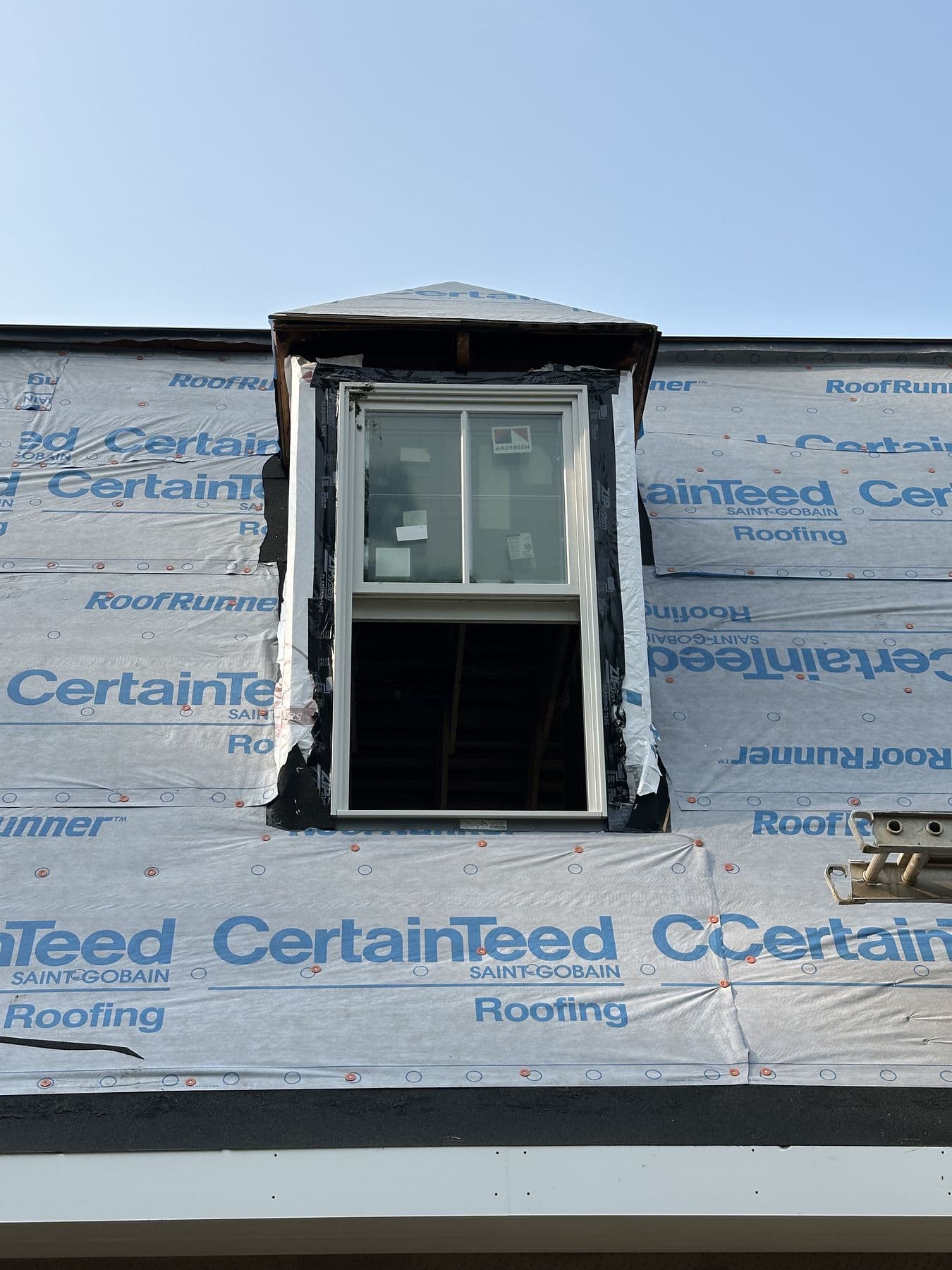 Finished dormer window with white trim and a small hip roof, roof underlayment still exposed