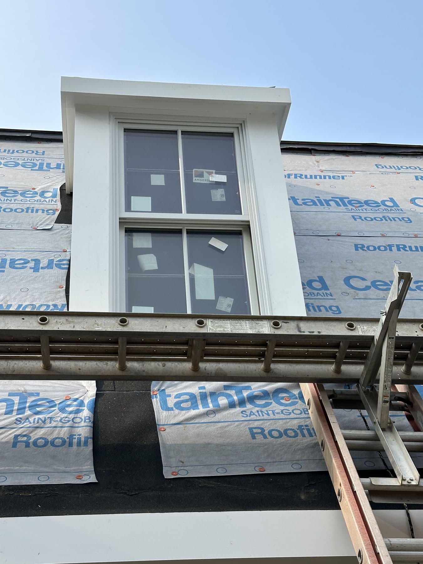 Dormer face trimmed in white with the window installed and underlayment around it