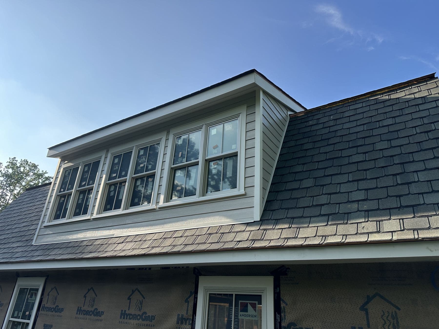 Long shed dormer with a row of new windows finished in gray lap siding above the stone wall
