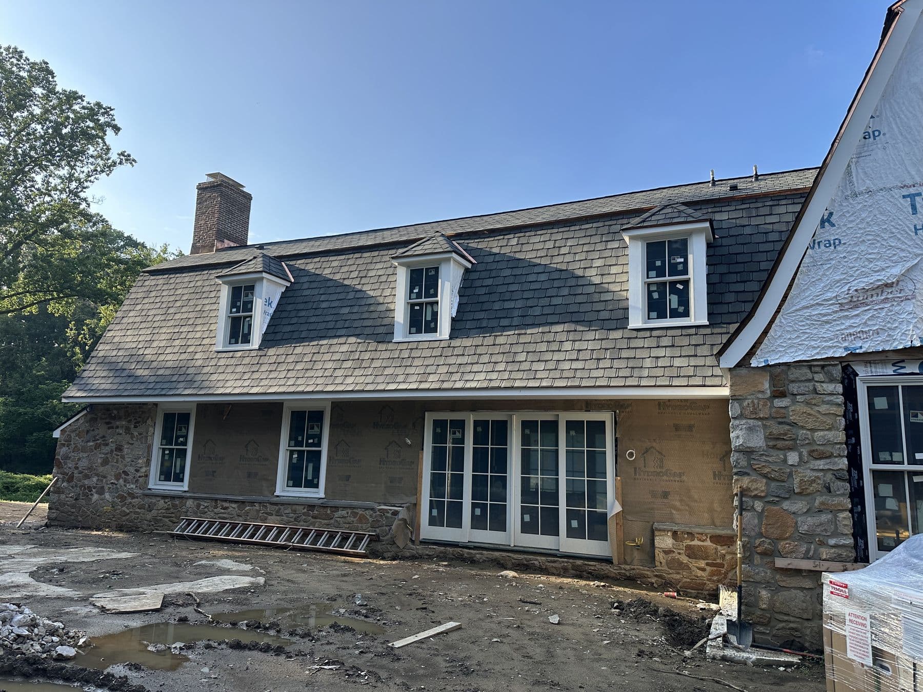 Rear of the stone house with new dormers on the roof and the addition wrapped in housewrap