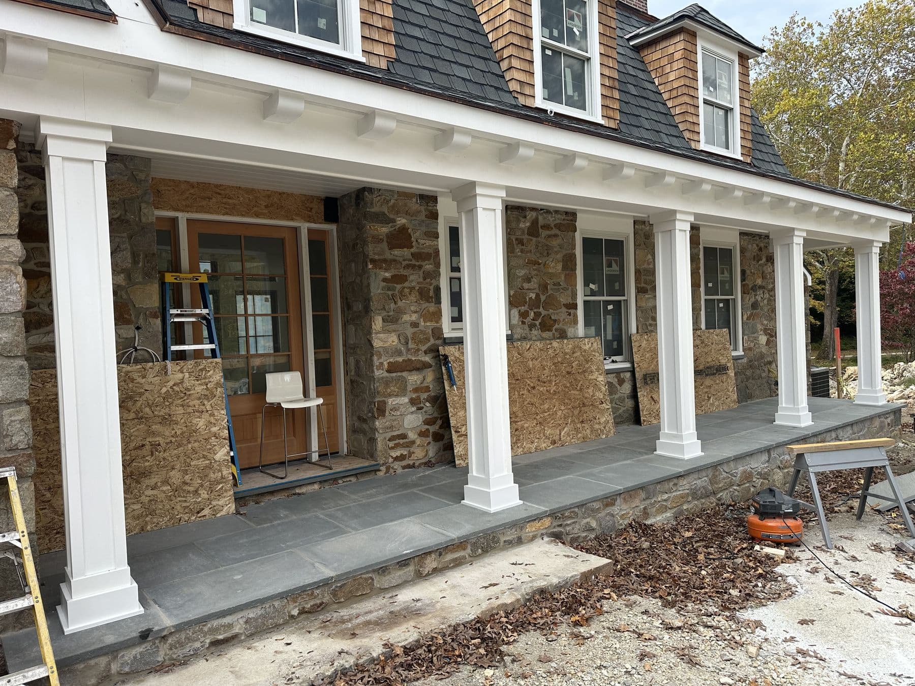 Front porch of the stone house with white square columns and a beadboard ceiling