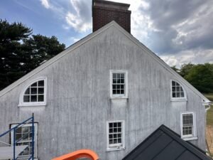 Weathered gray stucco gable with arched and rectangular white windows and a brick chimney before renovation