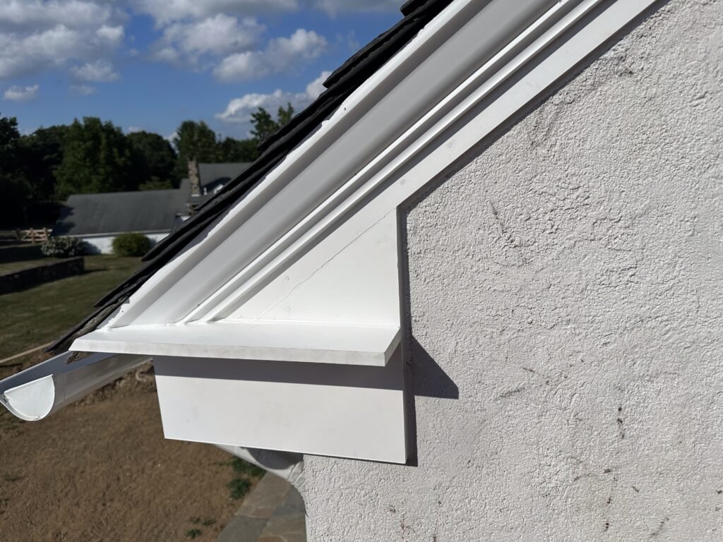 White rake trim and half-round gutter detail at the eave of a stucco home with a slate roof