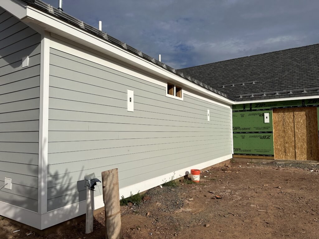 Sage green fiber cement lap siding with white trim next to a section still in ZIP System sheathing