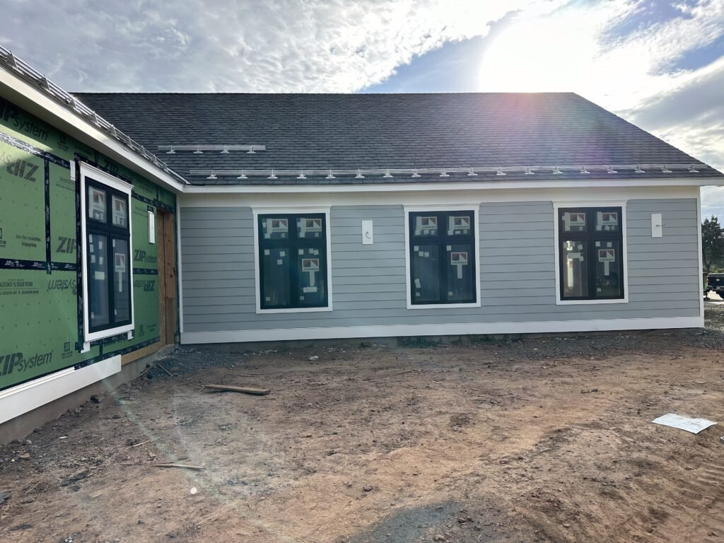 Single-story home with gray fiber cement lap siding, black windows, and white trim under construction