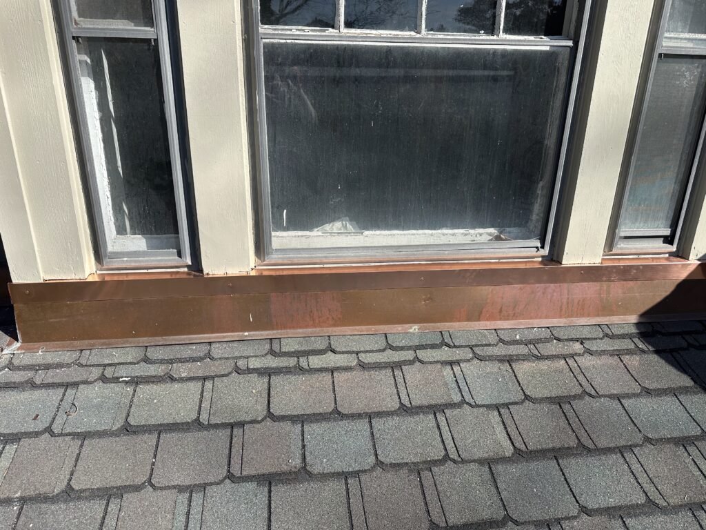 New copper sill pan flashing installed beneath a window above a slate shingle roof