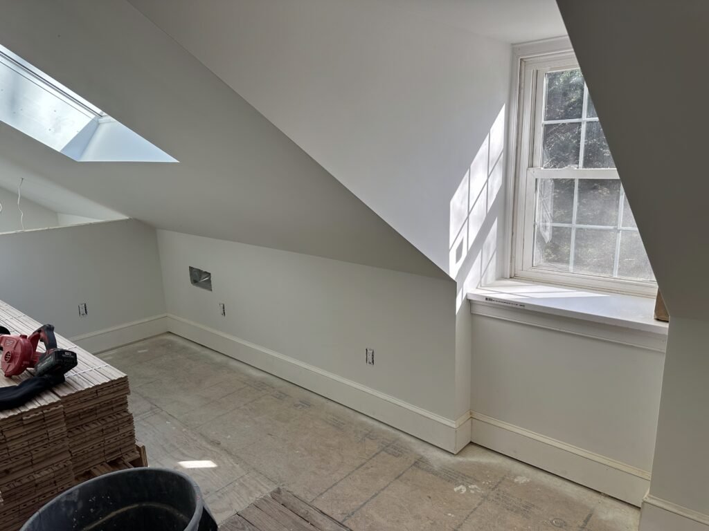 Attic room with a sloped ceiling, skylight, and white double-hung window during interior finishing
