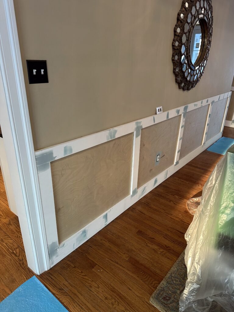 Board-and-batten wainscoting frames being installed on a hallway wall over hardwood flooring