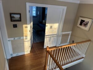 Top of an oak staircase with wood handrail and white balusters beside a finished living room