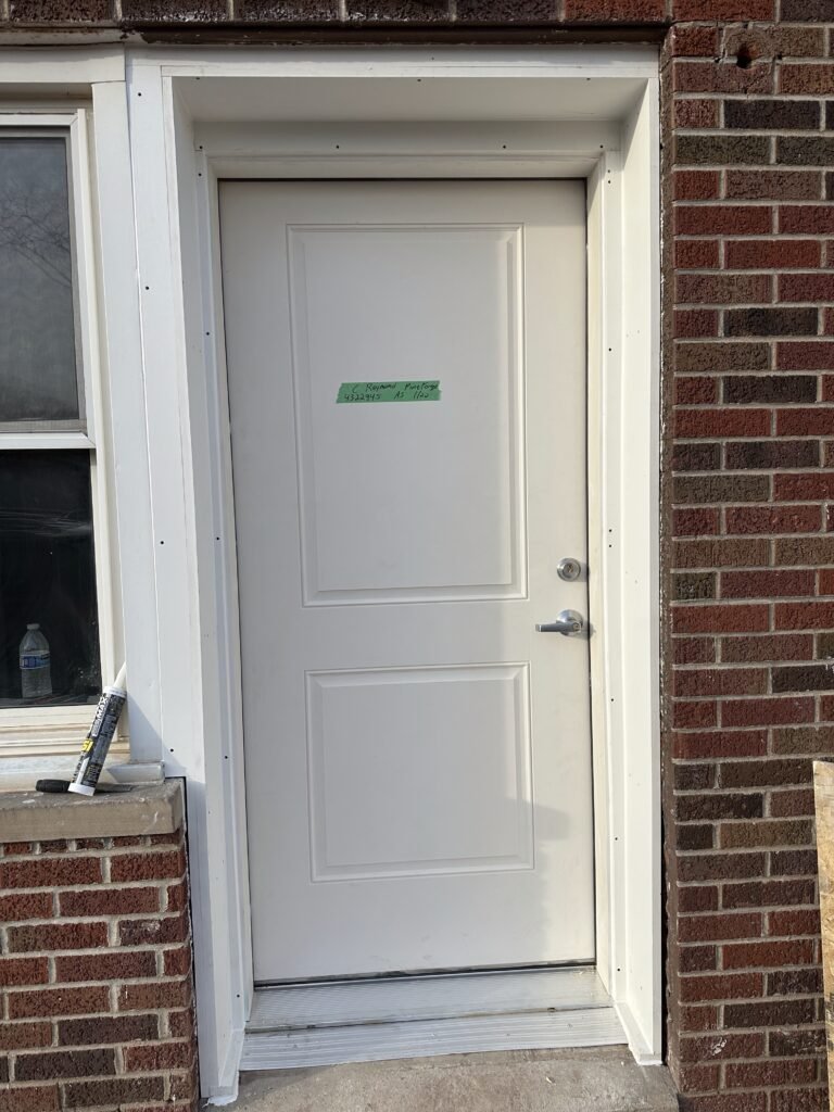 New white two-panel steel door with fresh trim installed in a red brick wall