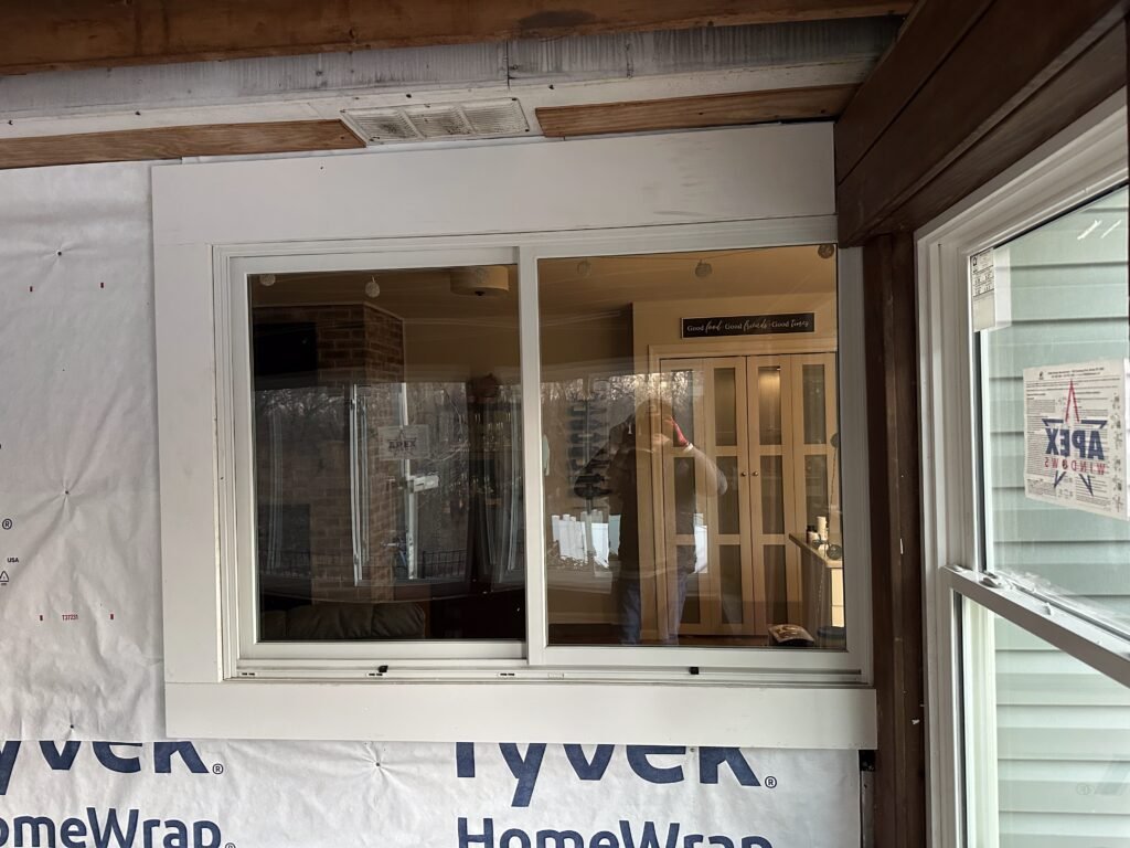New white sliding window in a Tyvek-wrapped wall looking into a finished kitchen interior