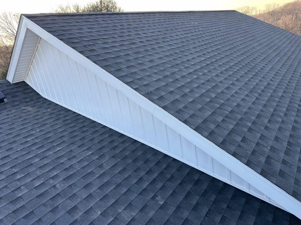 White board-and-batten gable return meeting a gray architectural shingle roof, aerial view