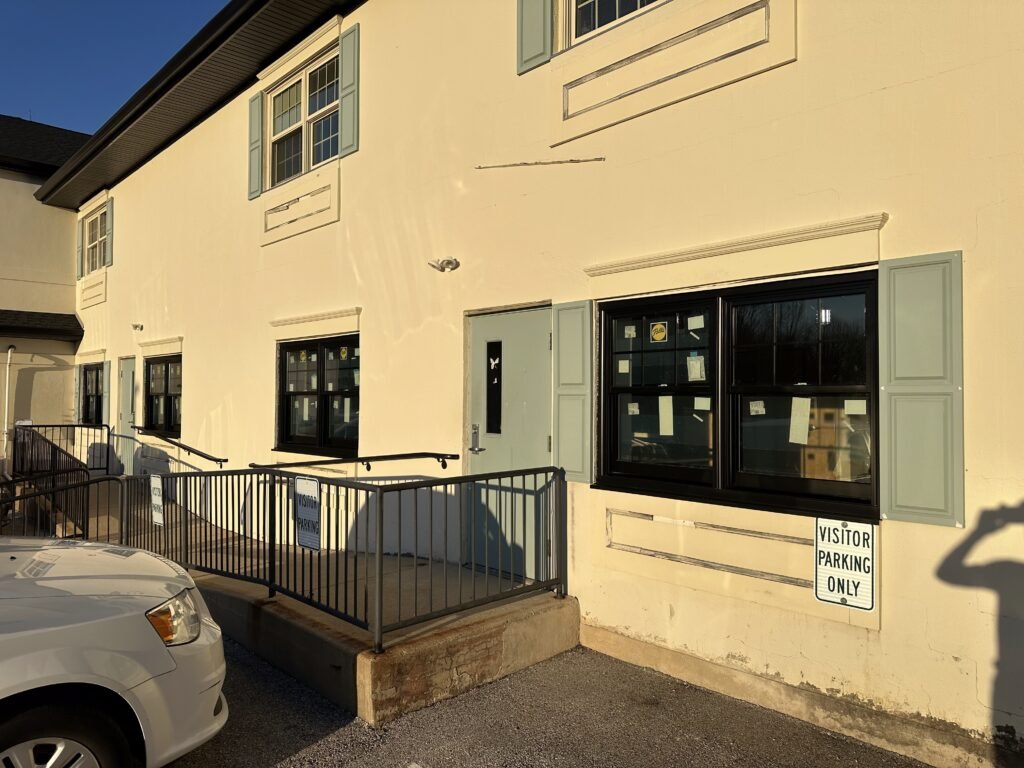 Cream stucco commercial building with black windows, sage shutters, and an accessible entry ramp