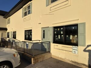 Cream stucco commercial building with black windows, sage shutters, and an accessible entry ramp