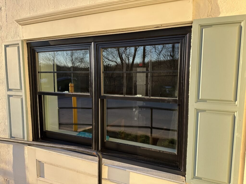 Black double-hung windows with sage shutters and a decorative cornice on a cream stucco commercial building