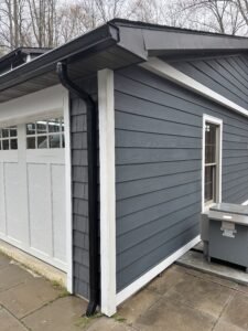 Charcoal fiber cement lap siding with shake accent, white trim, and black gutter at a garage corner
