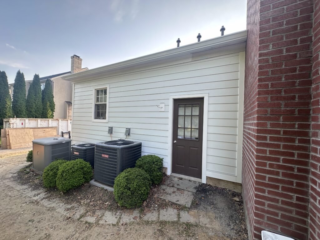 Cream lap siding with a white gutter and a brown side door on a home addition, AC units alongside