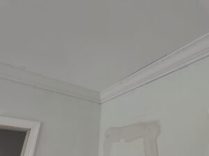 White crown molding installed at the ceiling line of a pale green room during interior finishing