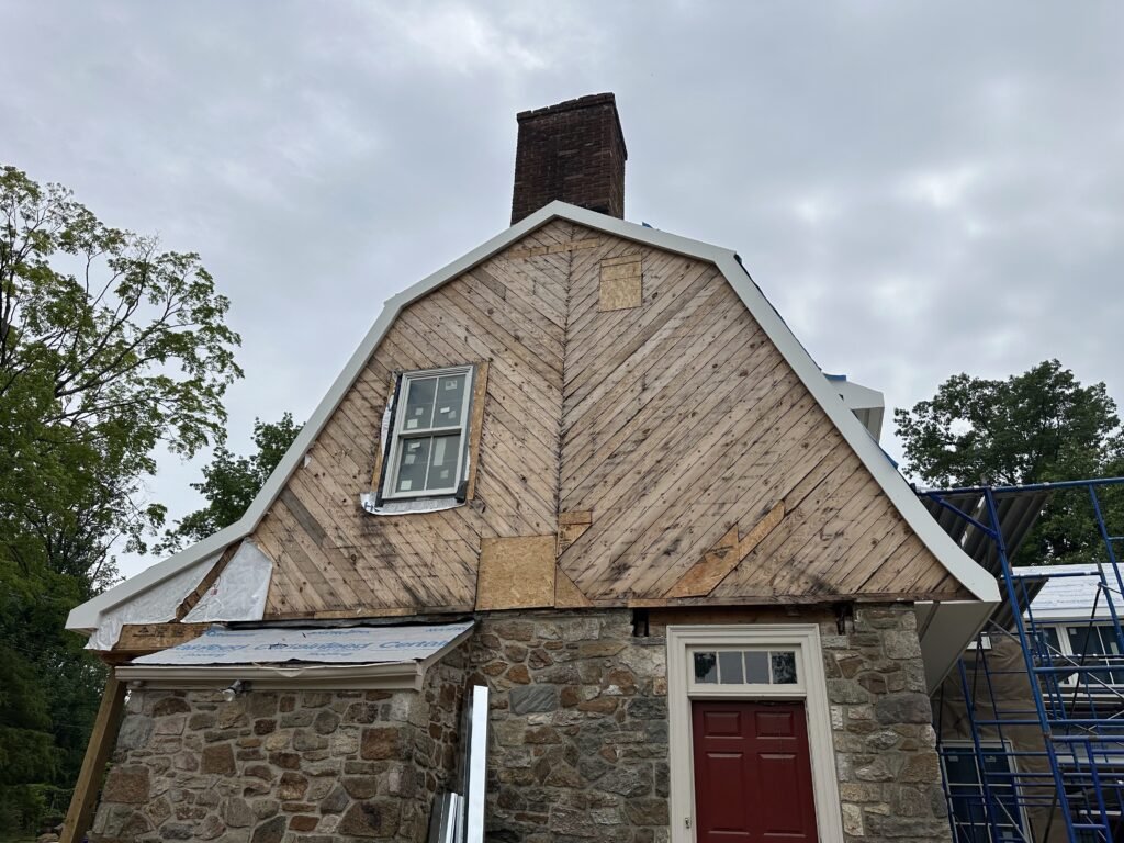 Gambrel gable with old diagonal plank sheathing exposed over a fieldstone base during a re-siding project