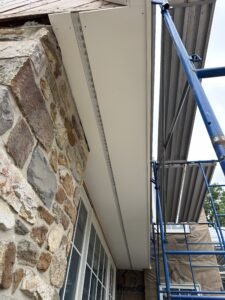 White PVC soffit and frieze board being installed at the eave above a fieldstone wall