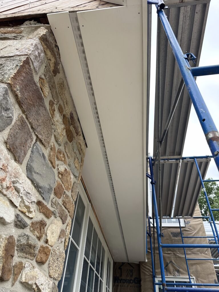 White PVC soffit and frieze board being installed at the eave above a fieldstone wall