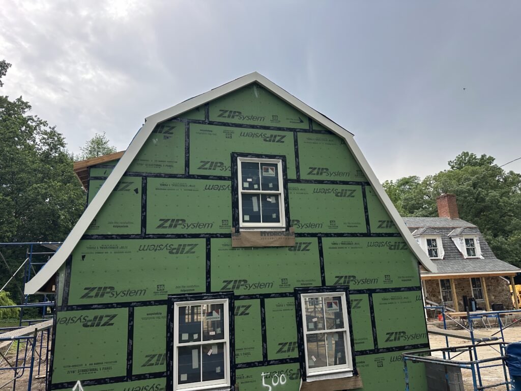 Gambrel gable in ZIP System sheathing with new white rake trim and windows during construction