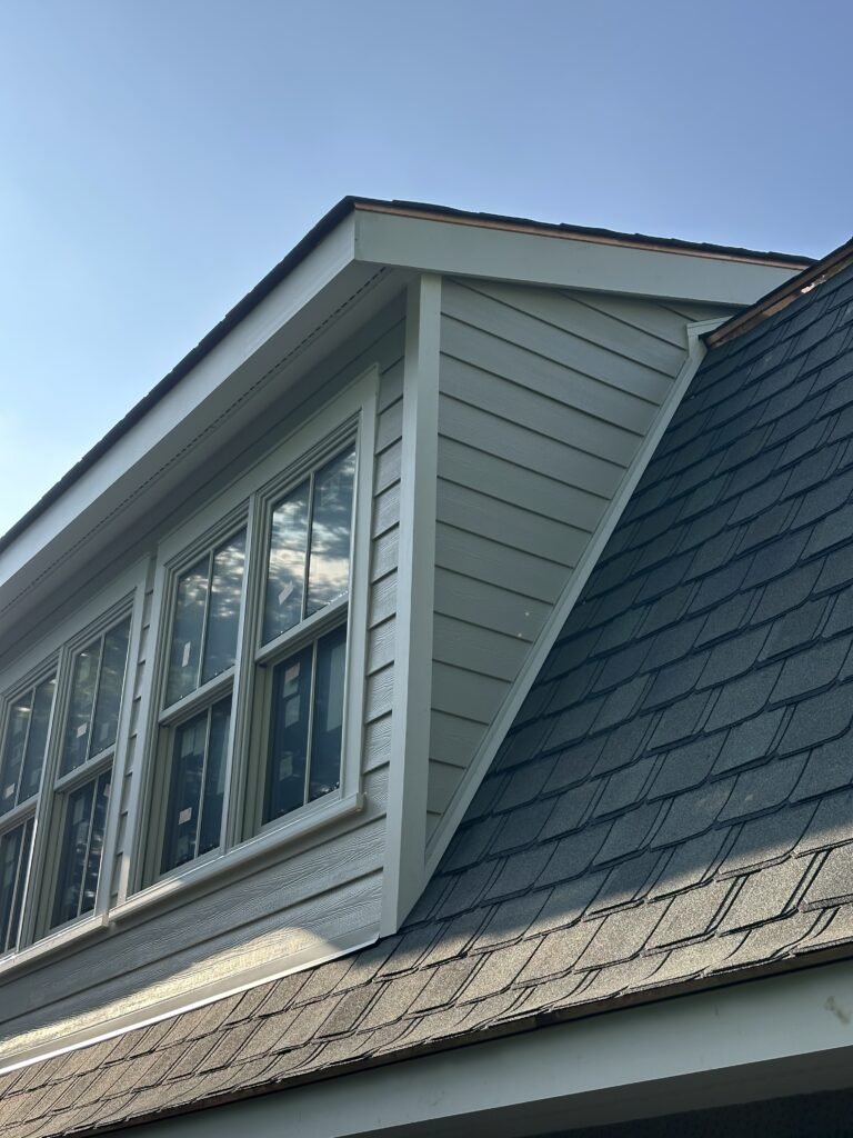 Gray clapboard shed dormer with a bank of windows and copper drip edge on a faux slate roof