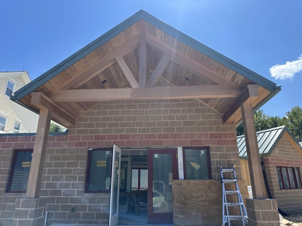 Covered entrance with a cedar timber-truss gable and standing-seam roof over a split-face block wall