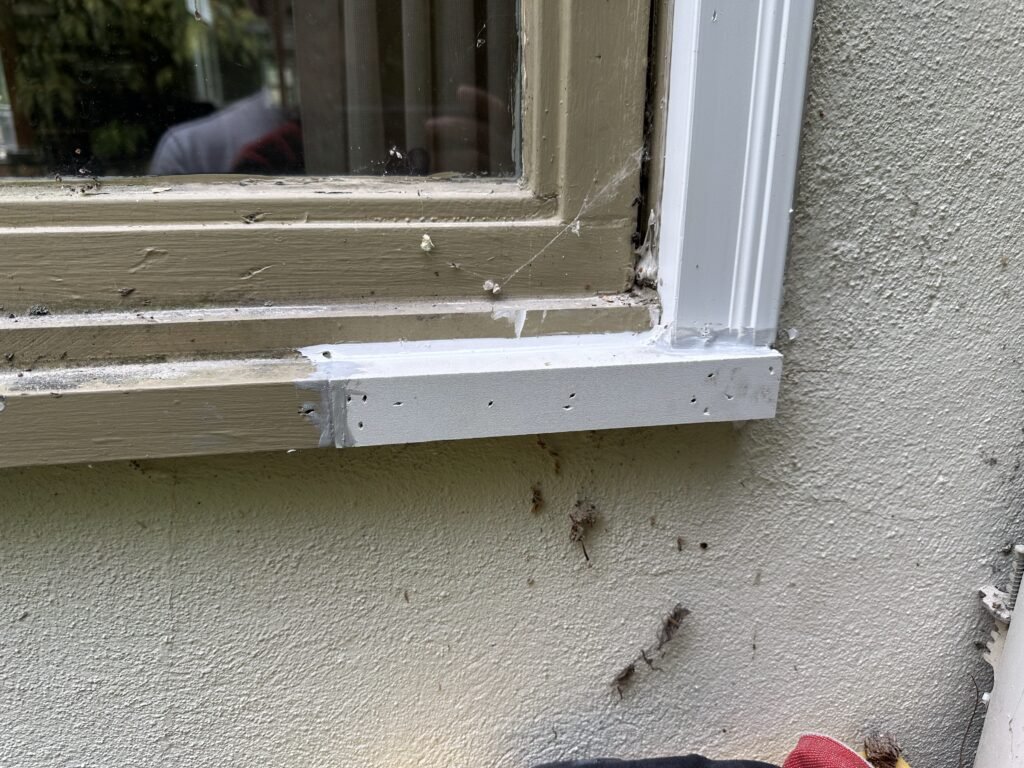 New white painted window sill installed over old trim on a green stucco wall during repair