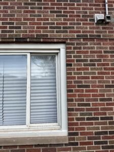 Old white sliding window and dryer vent on a red brick home before window replacement