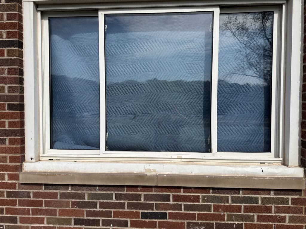 Old white aluminum sliding window on a red brick home before replacement