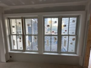 Four-unit white Andersen double-hung window bank with built-up trim overlooking a stone patio