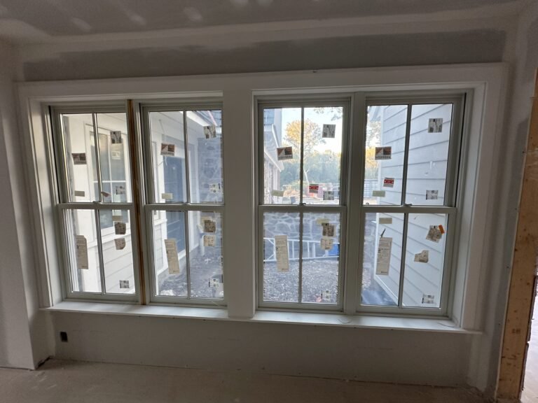 Four-unit white Andersen double-hung window bank with built-up trim overlooking a stone patio