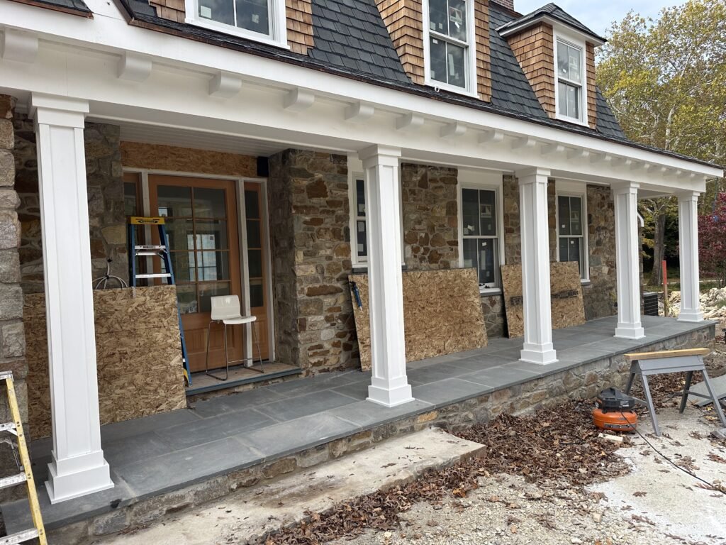 Covered front porch with white columns and bluestone floor on a stone home under construction