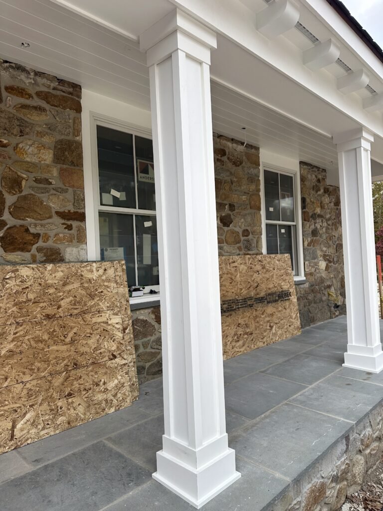 White porch columns and beadboard ceiling over a bluestone floor on a fieldstone home under construction