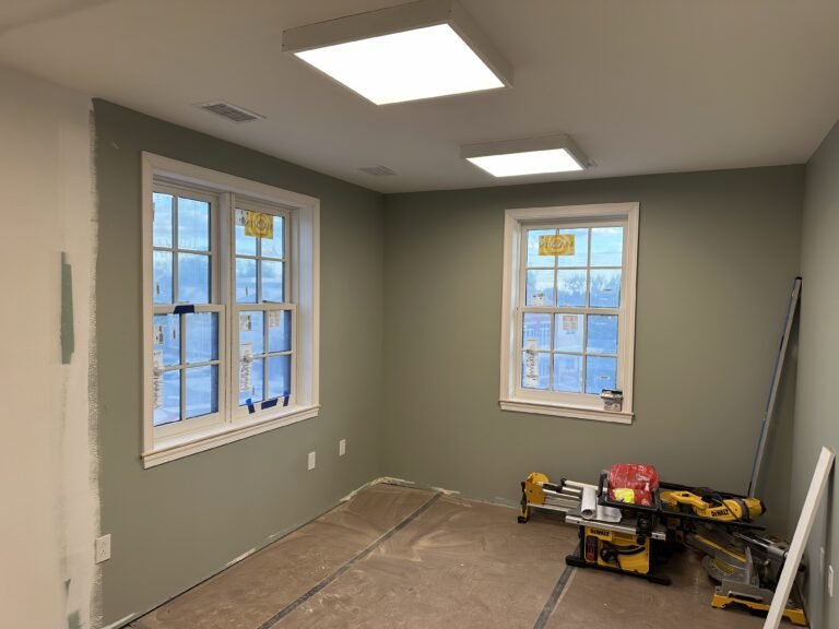 Sage green room with white Andersen double-hung windows and a miter saw during trim work