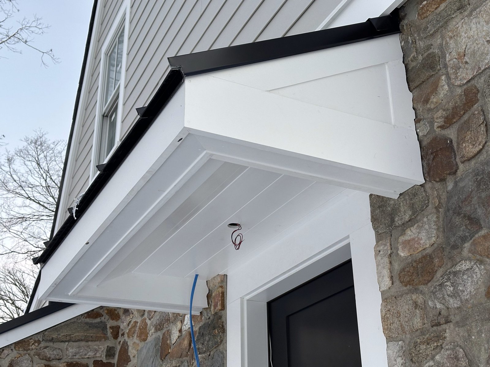 Custom entry portico Berwyn PA with white beadboard soffit, V-groove fascia panels, decorative bracket, and black metal drip edge on a stone home by D&E Mako Renovation