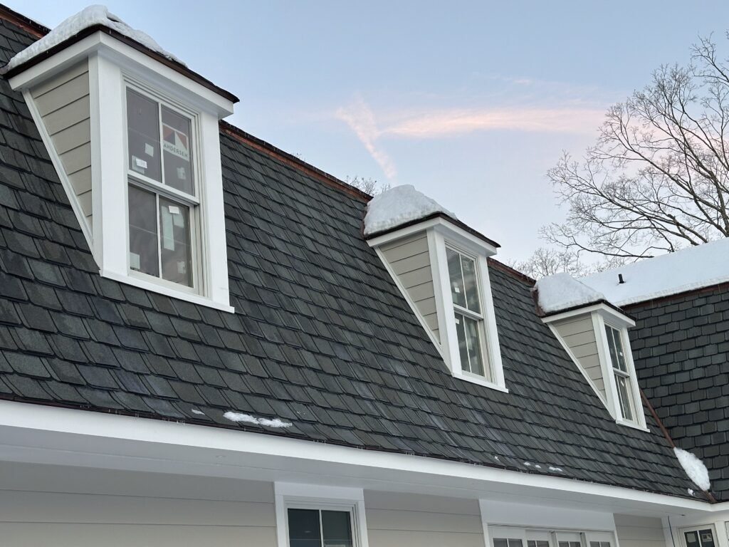 Three shed dormers with white-trimmed windows on a faux slate mansard roof with copper drip edge in winter