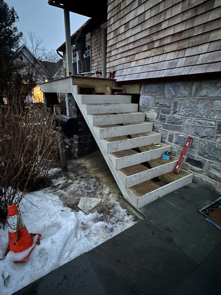 Open stair stringers under construction beside a cedar shake and stone home at dusk