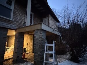 Cedar shake home with stone pier columns supporting a deck under construction at dusk