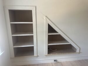 White built-in bookcases fitted to a sloped ceiling, one rectangular and one triangular, with trim
