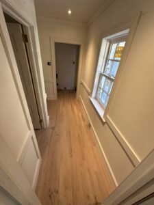 Finished interior hallway with refinished oak flooring, white trim, and a divided-lite window