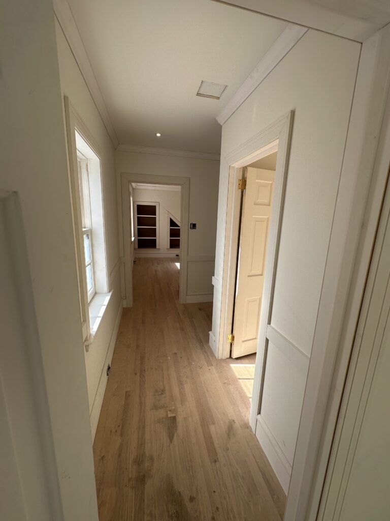 Interior hallway mid-renovation showing new white oak hardwood floors, chair rail trim, Marvin window, and bathroom tile floor visible through doorway in Downingtown PA Chester County
