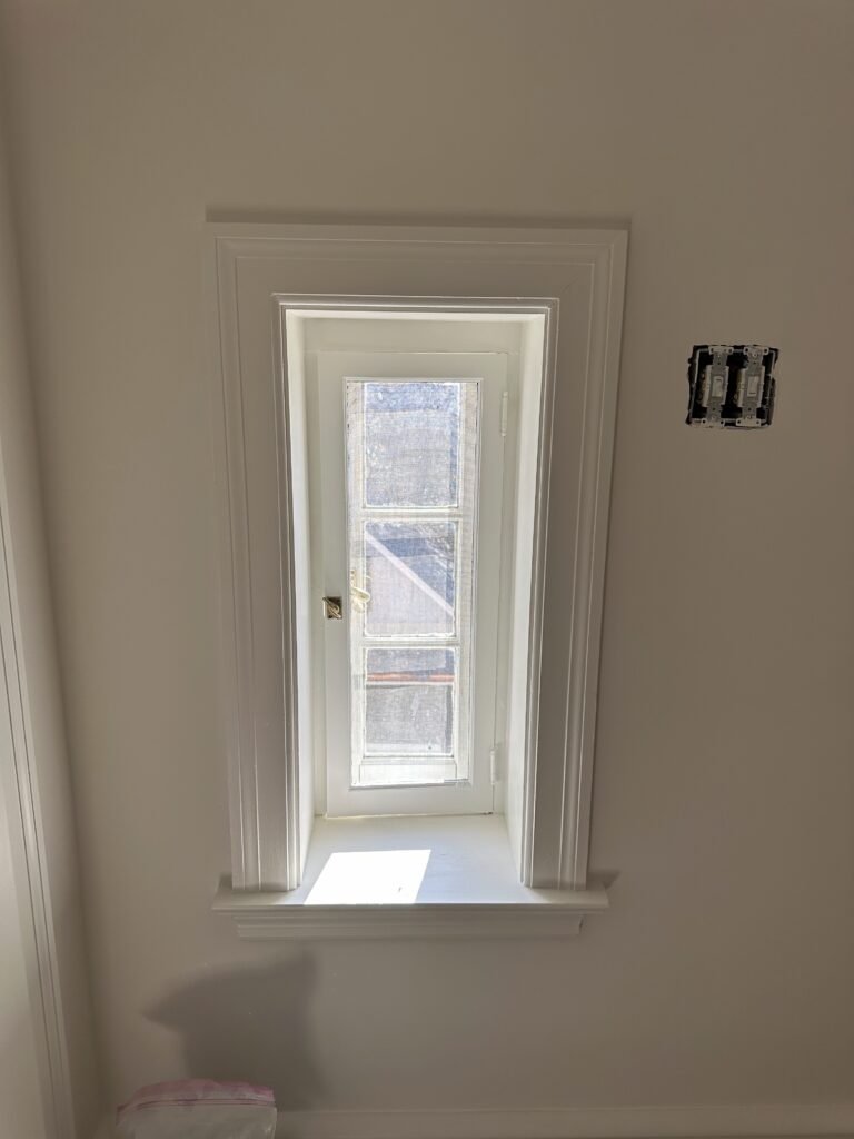 Small three-lite window in a deep white-trimmed reveal with a molded sill in a finished room