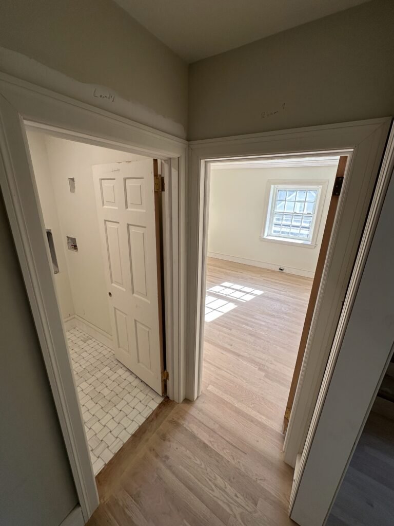 Finished interior hallway with white trim, a tiled bathroom, and a bedroom with refinished oak flooring