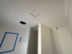 White crown molding around a recessed ceiling and beam with a black vent during interior finishing