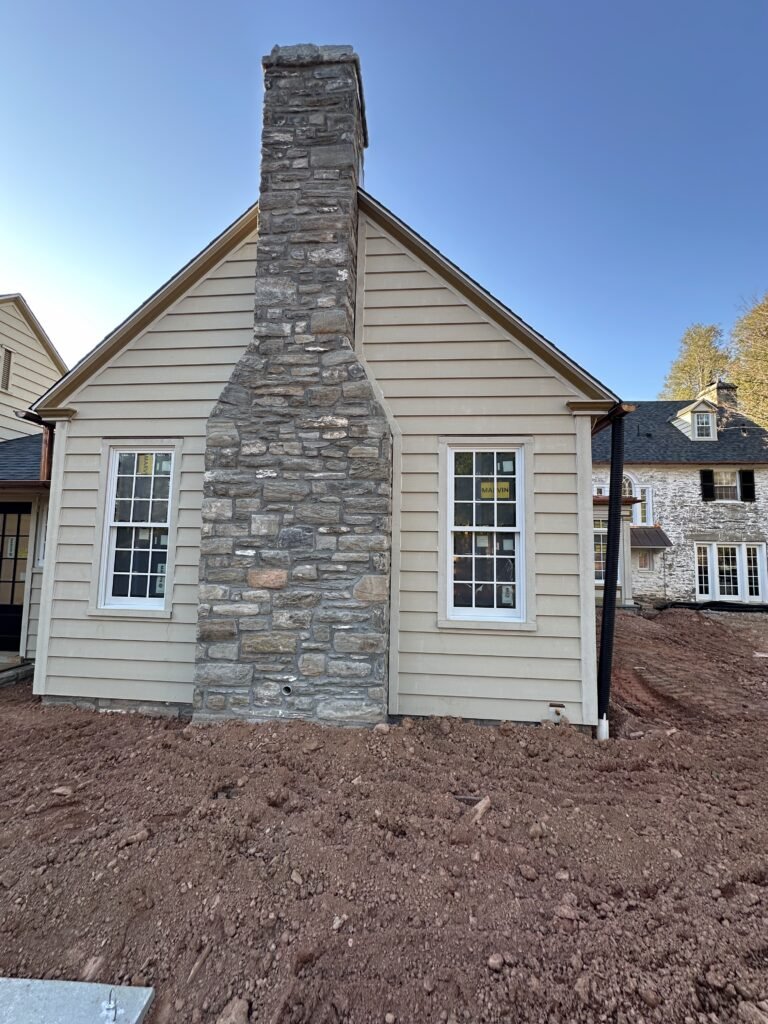 Cream lap siding gable with a tall fieldstone chimney and white double-hung windows